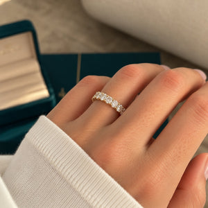 A close-up of a hand wearing a delicate diamond eternity ring on a gold band, with a teal jewelry box in the blurred background.