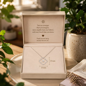 Necklace in a decorative box with an inspirational message, surrounded by plants.