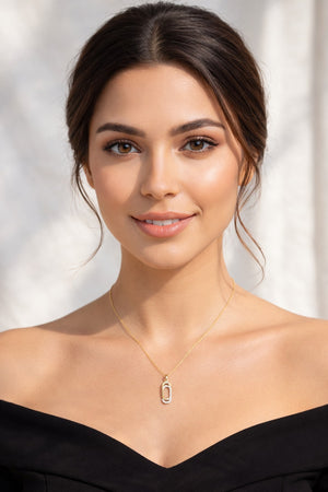 Woman wearing a black off-shoulder top and gold necklace with a pendant against a light background