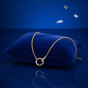 Gold necklace with a circular pendant on a blue cushion against a blue background