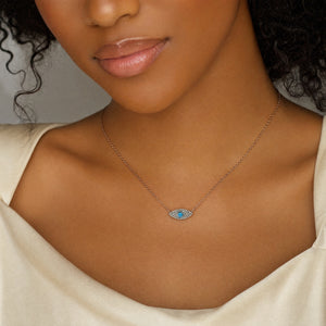 A close-up of a model wearing a delicate silver chain necklace with a small evil eye pendant featuring blue and white accents.