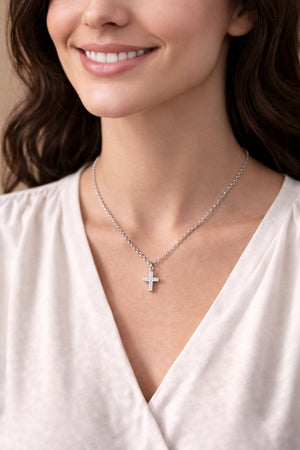 Woman wearing a silver necklace with a cross pendant on a neutral background