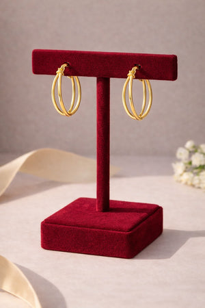 Gold hoop earrings on a red velvet stand with a neutral background