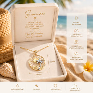 Gold necklace with palm tree design in a decorative box on a beach-themed background