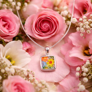 Silver pendant with floral design on a bed of pink and white flowers