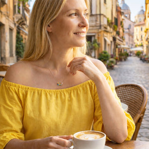 Woman in a yellow top holding a coffee cup in an outdoor setting with buildings and street in the background.