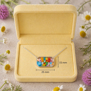 Necklace with a colorful pendant in a yellow jewelry box, surrounded by flowers.
