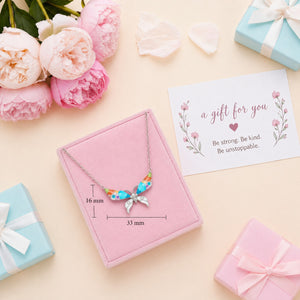 Necklace with floral design in a pink jewelry box, surrounded by flowers and gift boxes on a beige background.