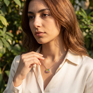 Woman wearing a necklace with a colorful pendant against a green leafy background