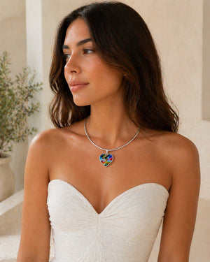Woman wearing a white strapless dress and a colorful heart-shaped necklace indoors.