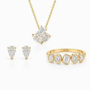 Elegant yellow gold jewelry set featuring pear and emerald-cut diamonds, including stud earrings, a pendant necklace, and a modern multi-stone ring on a light gray background.