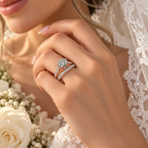 A close-up lifestyle shot of a woman's hand wearing a rose gold and white gold engagement ring with a diamond flower center, set against a soft background of white lace and roses.