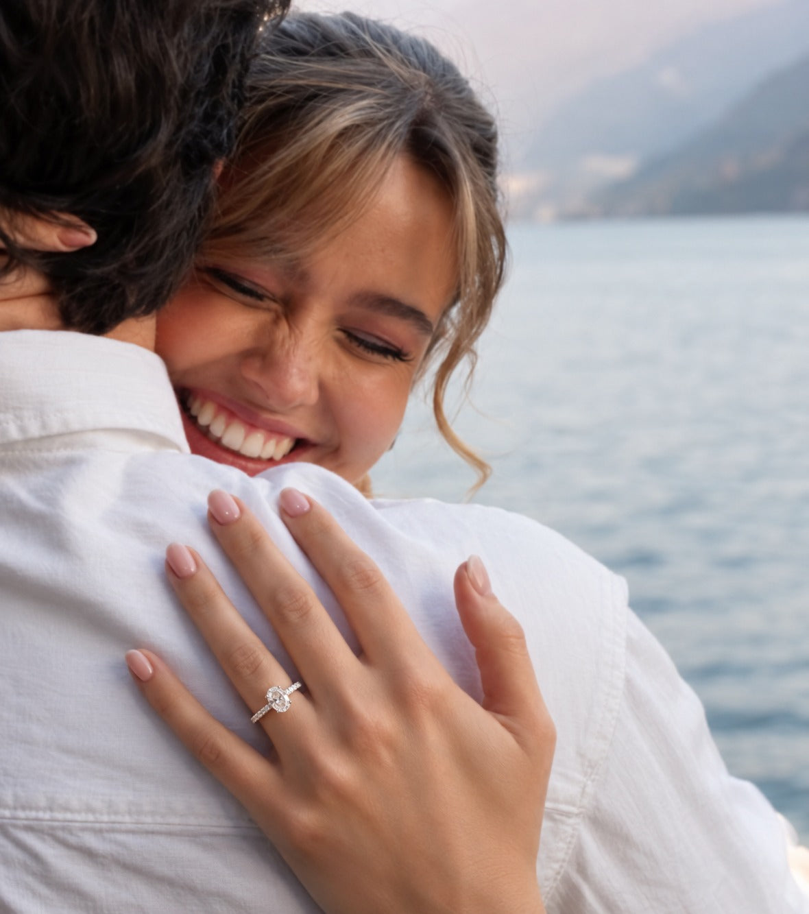 An oval diamond engagement ring in a silver-colored metal setting, featuring a halo of small diamonds and a pavé band with round diamonds, shown on a plain white background.