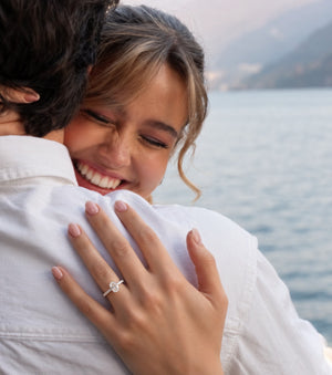 An oval diamond engagement ring in a silver-colored metal setting, featuring a halo of small diamonds and a pavé band with round diamonds, shown on a plain white background.