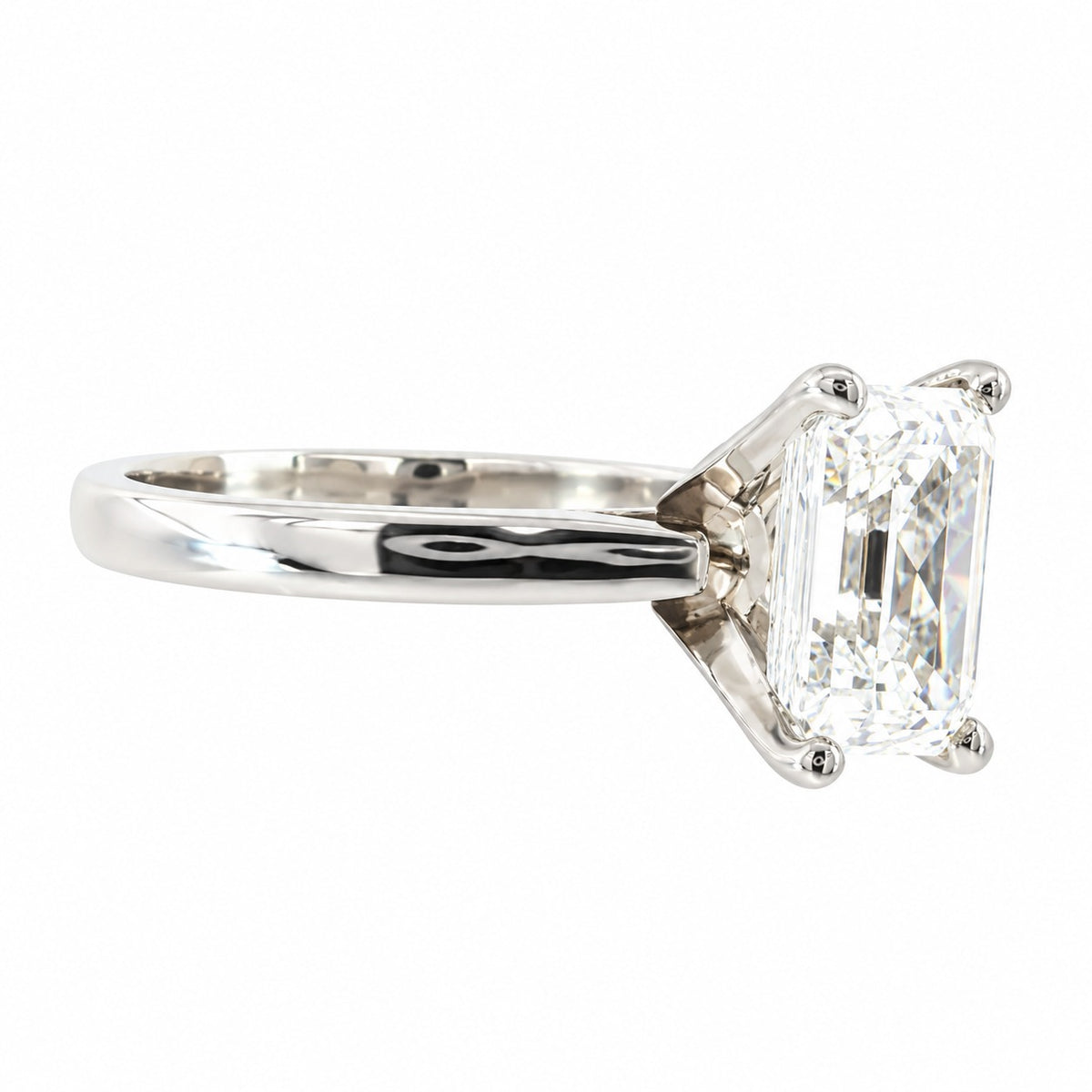 An emerald-cut diamond ring in a polished silver-colored metal setting, shown from a side profile view against a plain white background.