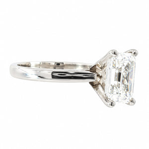 An emerald-cut diamond ring in a polished silver-colored metal setting, shown from a side profile view against a plain white background.