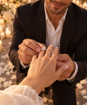 An engagement ring featuring a brilliant round-cut diamond center stone in a four-prong setting, with a pavé band set with small round diamonds