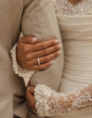 Bride wearing a 14K yellow gold wedding band featuring 11 brilliant round lab-grown diamonds totaling 0.98 CT, elegantly resting her hand on the groom’s beige suit during a romantic wedding moment.