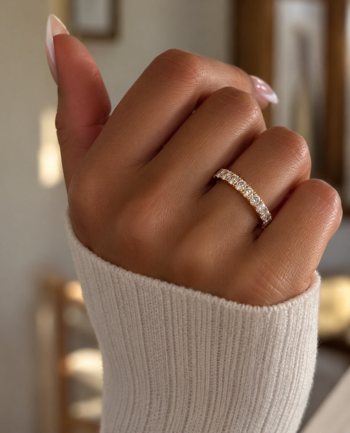 Close-up lifestyle photo of a woman wearing a 14K yellow gold wedding band featuring 11 round lab-grown diamonds totaling 0.98 CT, paired with a cozy ivory knit sweater and soft, warm lighting.