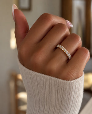 Close-up lifestyle photo of a woman wearing a 14K yellow gold wedding band featuring 11 round lab-grown diamonds totaling 0.98 CT, paired with a cozy ivory knit sweater and soft, warm lighting.