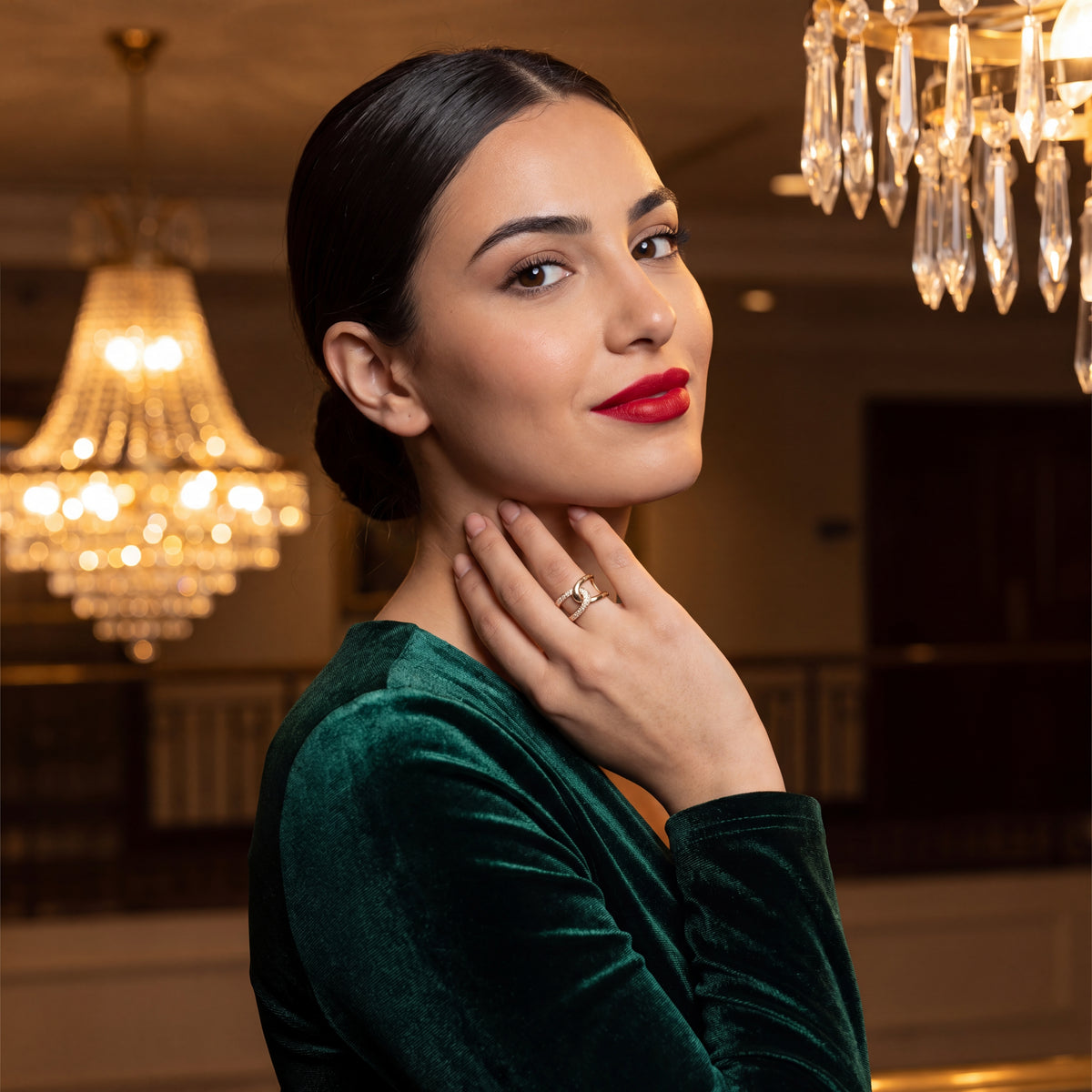 Woman in a green dress with red lipstick posing indoors with chandeliers in the background
