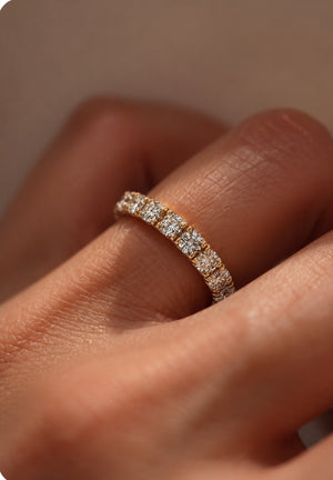A close-up of a yellow gold eternity ring set with small round diamonds worn on a person's finger.