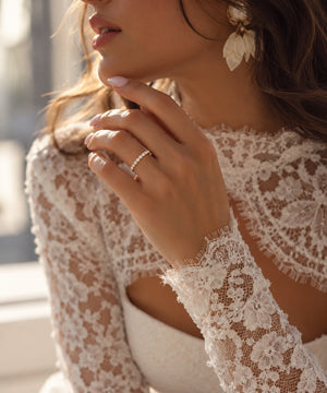 Close-up of a bride wearing a 14K yellow gold wedding band featuring 17 round lab-grown diamonds totaling 0.23 CT, with her hand near her face and an elegant lace wedding dress.