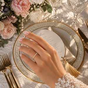 Delicate 14K yellow gold 0.23 CT lab-grown diamond wedding band worn on a bride's hand above an elegant wedding table with blush flowers and gold accents.