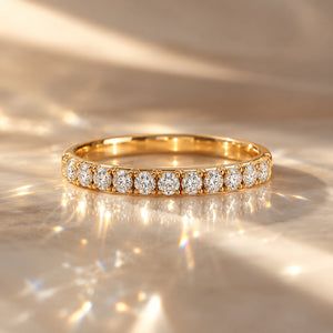 A gold eternity ring set with round brilliant-cut diamonds, resting on a shimmering gold surface with dramatic light reflections.