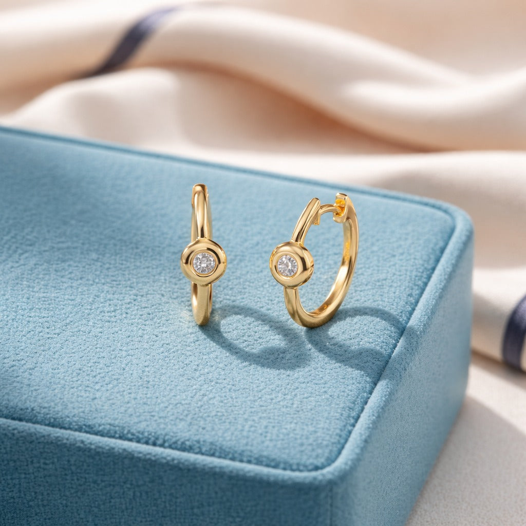 Gold hoop earrings with a central gemstone on a blue jewelry box.