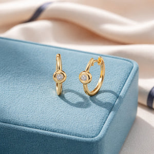 Gold hoop earrings with a central gemstone on a blue jewelry box.