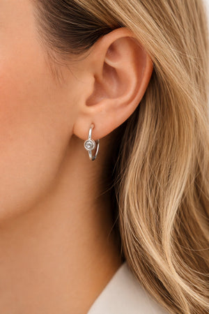 Close-up of a person wearing a silver hoop earring with a clear gemstone.