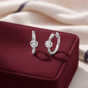 Silver hoop earrings on a burgundy jewelry box with a soft beige background
