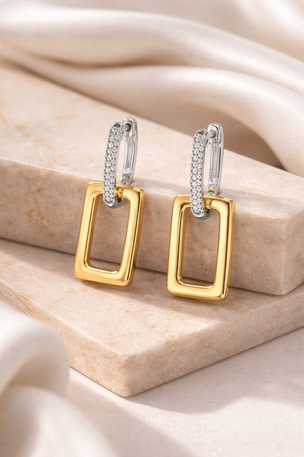 Gold and silver earrings on a beige stone surface