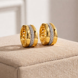 Gold hoop earrings with diamond accents on a beige surface