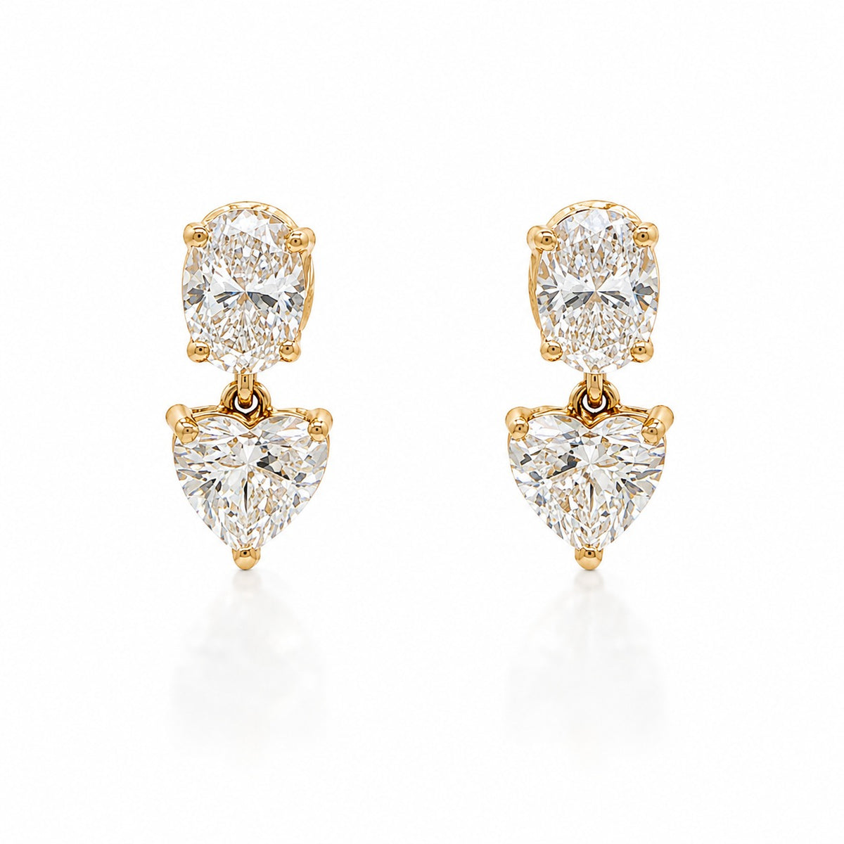 A pair of gold drop earrings featuring a round brilliant-cut diamond at the top and a heart-shaped diamond below, set in yellow gold on a white background.