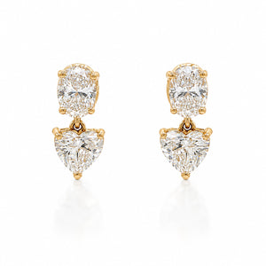A pair of gold drop earrings featuring a round brilliant-cut diamond at the top and a heart-shaped diamond below, set in yellow gold on a white background.