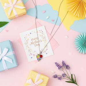 Necklace with heart and apple pendant on a 'Happy Mother's Day' card with gift boxes and decorative items.