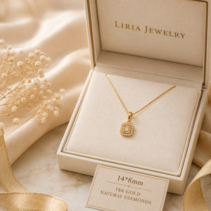 A gold pendant necklace displayed inside an open cream jewelry box. The pendant has a square shape with a halo of small clear stones and a central gold stone.