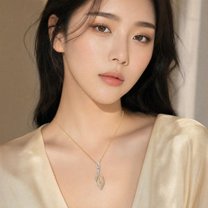 A close-up of a woman wearing a delicate gold leaf pendant necklace with a textured gold center and a silver bail, styled with a cream satin top.