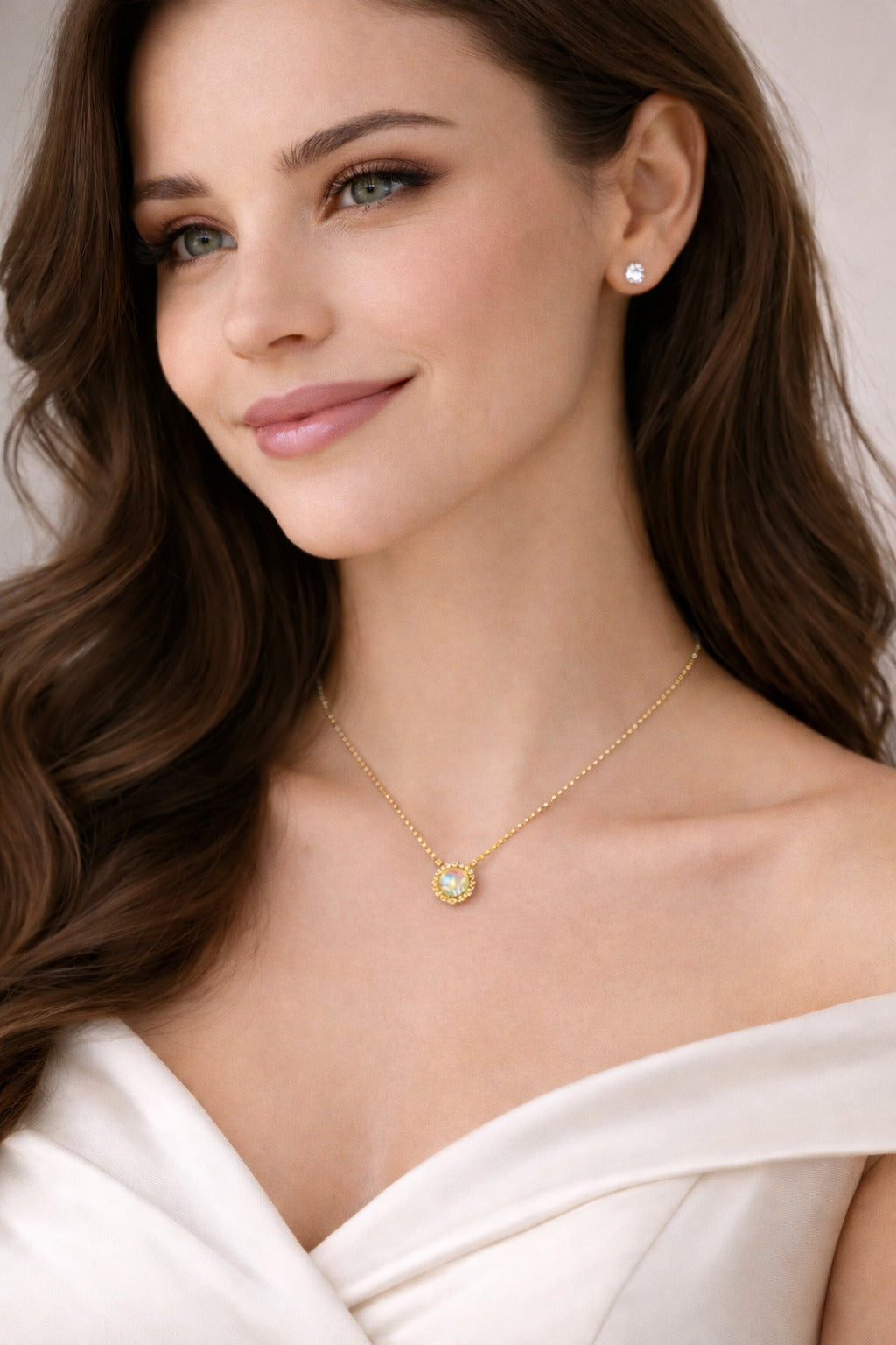 Woman wearing a gold necklace with a green gemstone against a neutral background