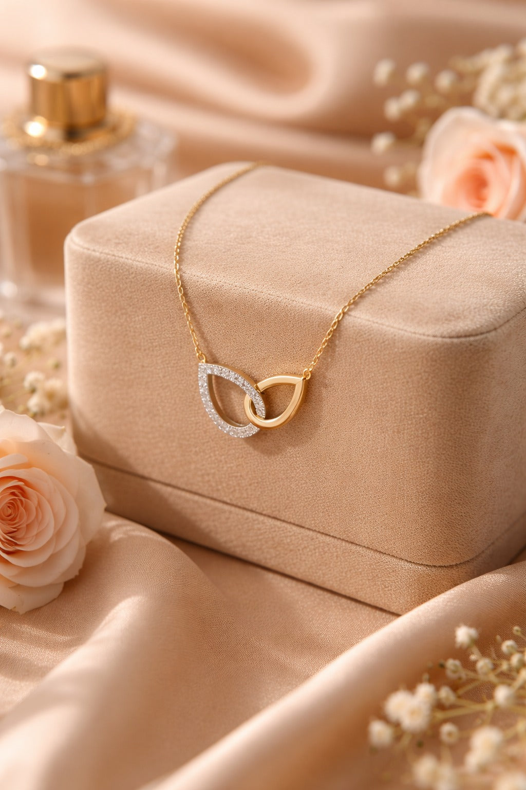 Gold necklace with interlocking rings on a beige jewelry box with flowers and perfume bottle in the background