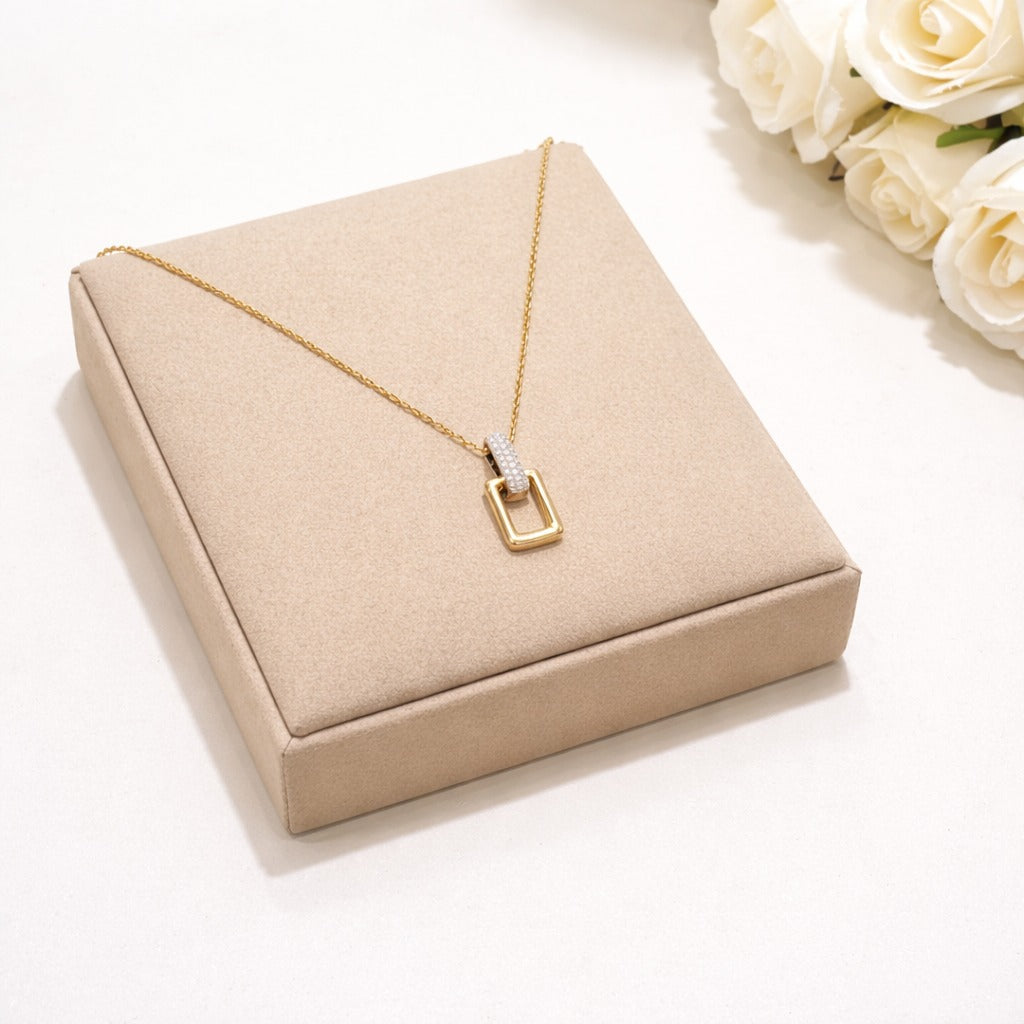 Gold necklace with a square pendant on a beige jewelry box with white roses in the background