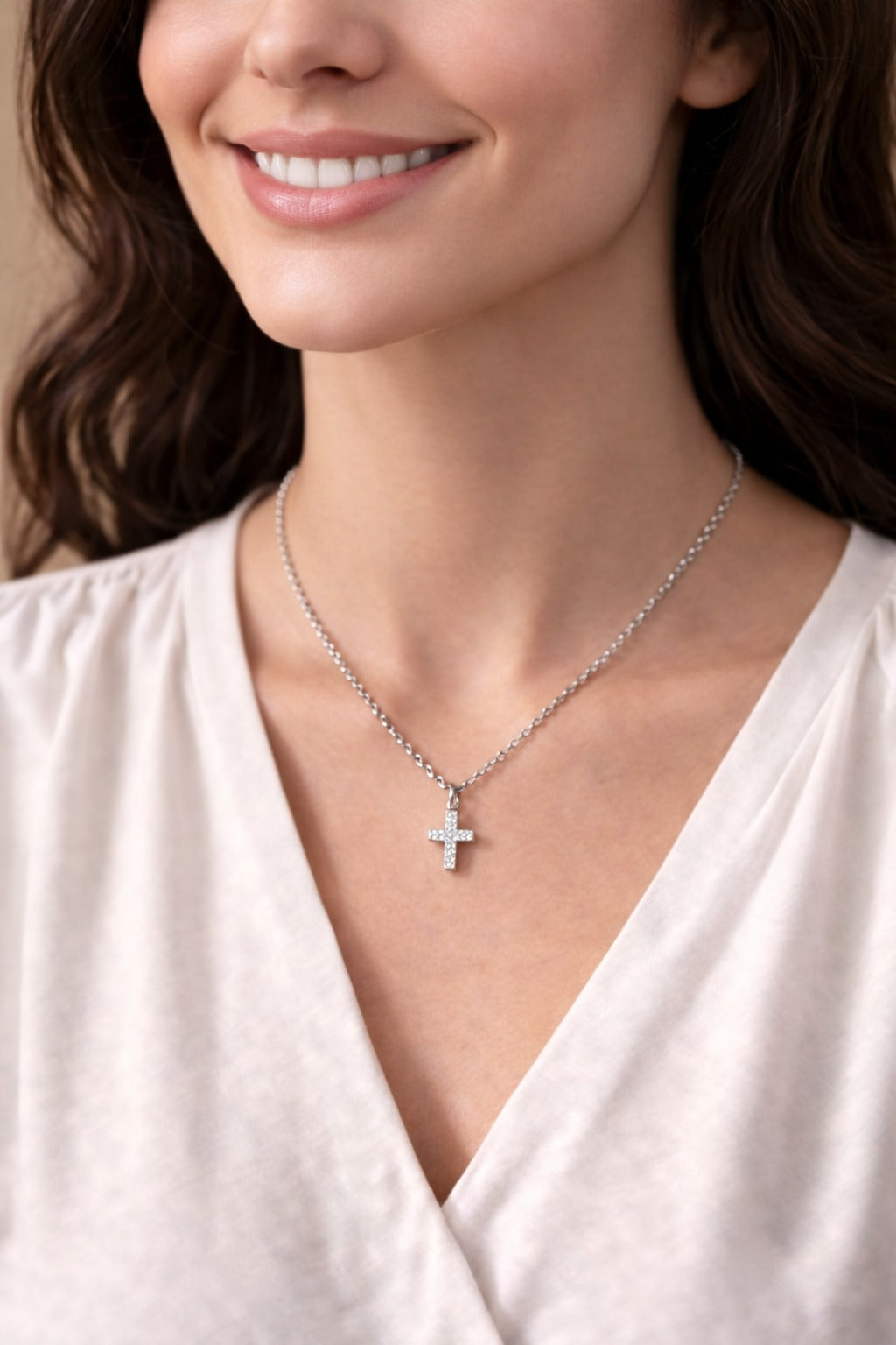 Woman wearing a silver necklace with a cross pendant on a neutral background