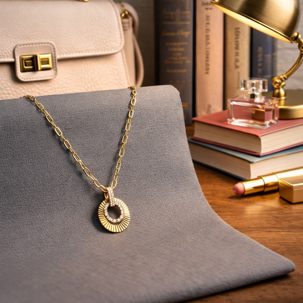 Gold necklace with a pendant on a gray surface, with books and a handbag in the background.