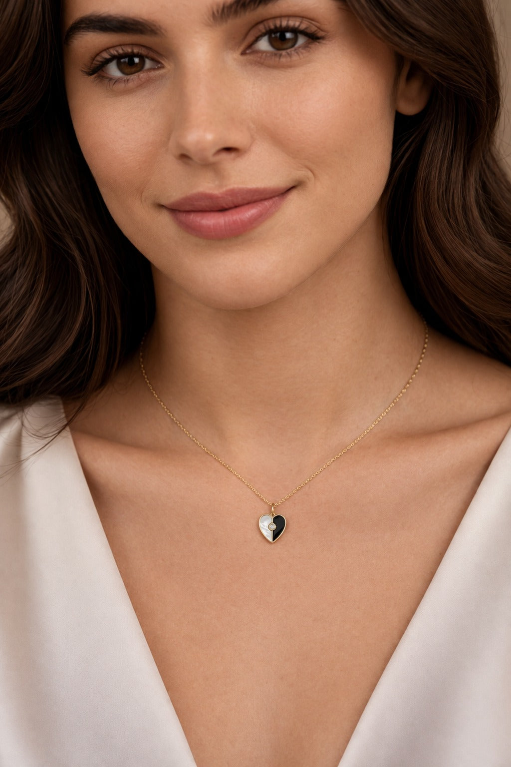 Woman wearing a delicate necklace with a heart-shaped pendant against a neutral background