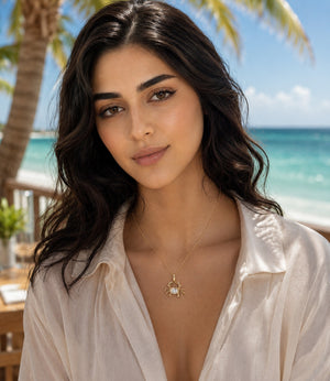 Woman wearing a delicate yellow gold crab pendant necklace with an oval diamond centerpiece, photographed on a tropical beach background with palm trees and ocean views.