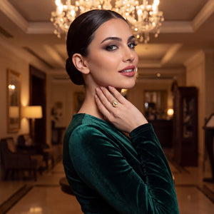 Woman in a green dress wearing a gold ring in a room with a chandelier.