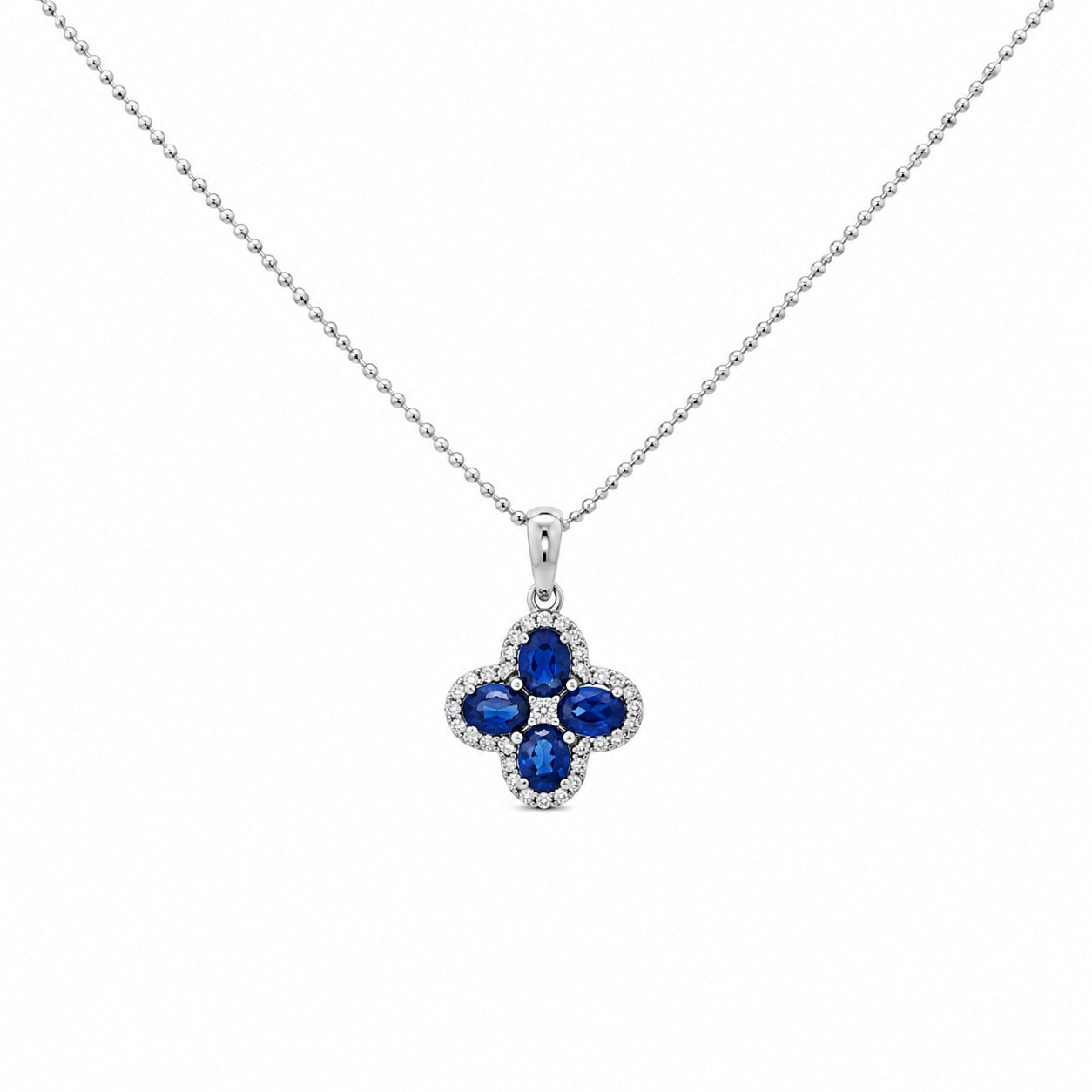 A 14K white gold bead chain necklace featuring a four-leaf clover pendant set with four vivid blue diamonds, accented by a sparkling halo of round white diamonds and a cluster at the centerdiamond , displayed on a clean white studio background.