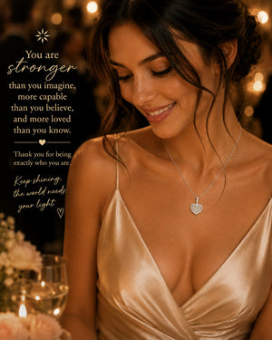 Woman wearing a necklace with a heart pendant in a warm, softly lit setting.